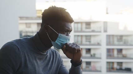 Lonely black man with medical mask on the balcony. Quarantine and mental health problems. High...