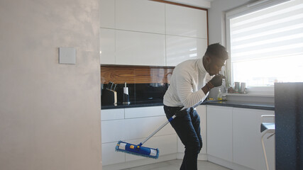 Happy handsome black man listening to the music and using broom as guitar. tidying up appartment. High quality photo