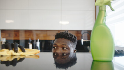 Black man cleaning kitchen. Surface reflects his face . High quality photo
