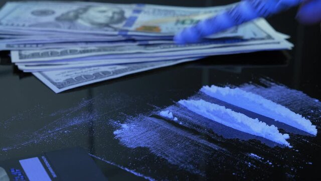 Addict is snorting cocaine or heroin white drug powder off black table with straw of US dollar banknote. Dope fiend is using drugs. Man sniffs line of amphetamines powder through money bill