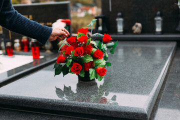Old woman laying down bouquet of artificial flower on a grave