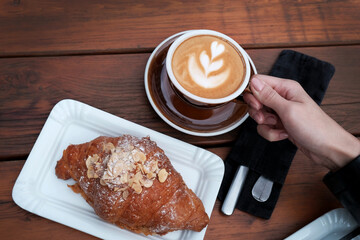 female hand holding a cup of coffee. Croissant and cappuccino on a wooden background. photo top view