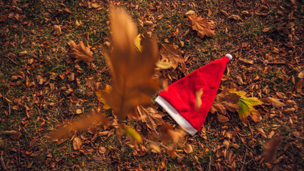 Holiday season is coming soon. A conceptual background photo of Santa Claus hat on yellow leaves in fall. Last day of autumn  and winter and christmas coming.