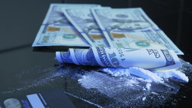 Man is pouring US 100 dollar bill on black table with lines of white drug powder. Rolled US banknote is lying on lines of drug powder. Cocaine, amphetamine, methamphetamine. Substance abuse concept
