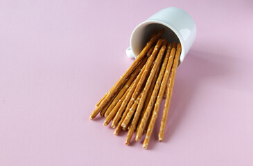 Bread sticks knocked over white cup on the pink background with copy space