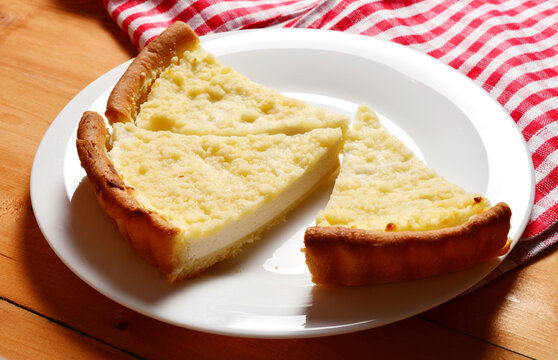 homemade curd cake on a white plate on a wooden table, next to a red checkered towel.