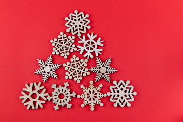 Christmas decorations. Fir tree made of small wooden snoflakes lyng on red background. Top view, flat lay, copy space for text