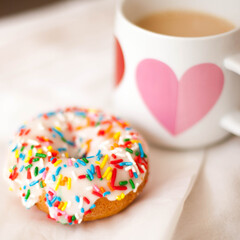 Single Vanilla Donut with Colorful Sprinkles and a Mug with a Heart with Coffee and Cream