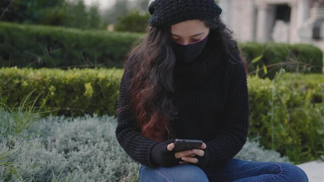 Vista de una adolescente en las calles de la Ciudad de México con ropa de abrigo y un cubrebocas en una tarde de otoño, covid19, una niña con su teléfono celular jugando o enviando un mensaje