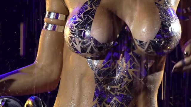 Hot nude female DJ playing music on a mixer console in a dark studio. A wet blonde dances among the raindrops. Woman's chest and torso with silver bodypainting close up. Slow motion.