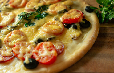 Homemade pizza with pepperoni, tomatoes, mozzarella and Basil, edible, on a wooden table with copy space for your text. Selective focus