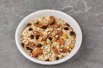 Healthy breakfast. Muesli or granola with dried fruits and pecans nuts in white bowl on gray stone table. Kinfolk style.