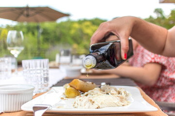Young girl spice a seafood. Drop of olive oil to spice a tasty sea bass with cooked leek and hazelnut. Perfect seafood meal.