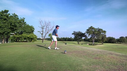 Asian Young adult male golfer driving tee off golf opening the shot tournament on green grass professional golf course wide shot, golfer swinging and hitting golf ball on beautiful golf club resort