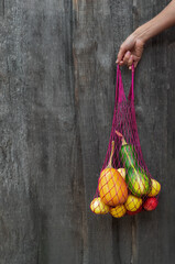 String bag with vegetables and fruits in the girl's hand on an old wooden background