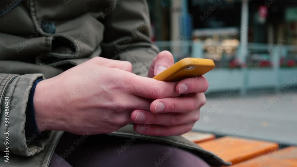 Poster the hands of a man in a gray autumn jacket actively use the touchpad of a smartphone in a yellow cas