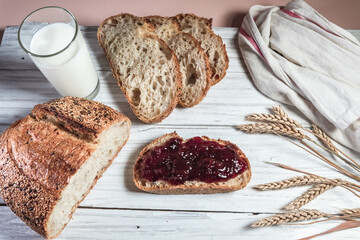 A glass of milk, sliced rustic bread and jam, on a white wooden board. Healthy food and farming concept