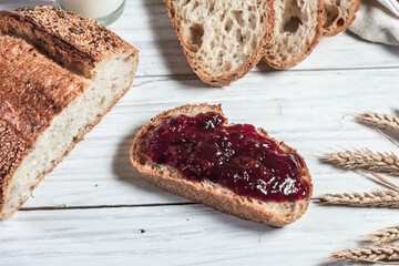 A slice of rustic bread smeared with jam on a white wooden board. Healthy food and farming concept