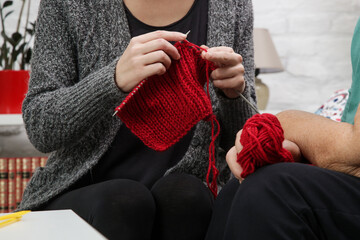 Grandomther and granddaughter spending quality  time together in creative and fun ways whilst strengthening their family bonds. Senior woman teaching young woman how to knit. Craft and DIY concept.