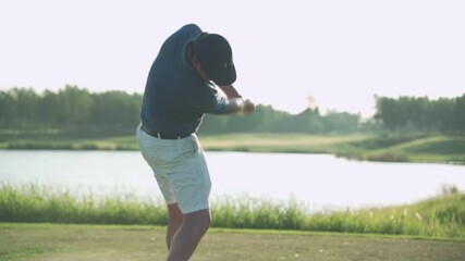 Young Asian adult male player driving golf on green grass professional golf course. Golfer with golf club, golfer swinging and hitting golf ball on beautiful course at sunset by the lake, sunset pond