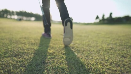 Low angle view following golfer walk on green grass golf fairway, out door sports, golf club resort, hot sunny day, healthy active lifestyle, tournament challenge, golfer legs walking rear view 