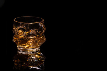  very beautiful faceted tumbler with whiskey and ice on a black background close with a place for text