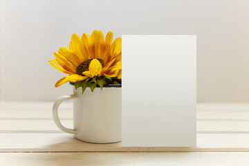 Postcard mockup with white cup and sunflowers. Empty card and enamel cup with space for text or print. White background.