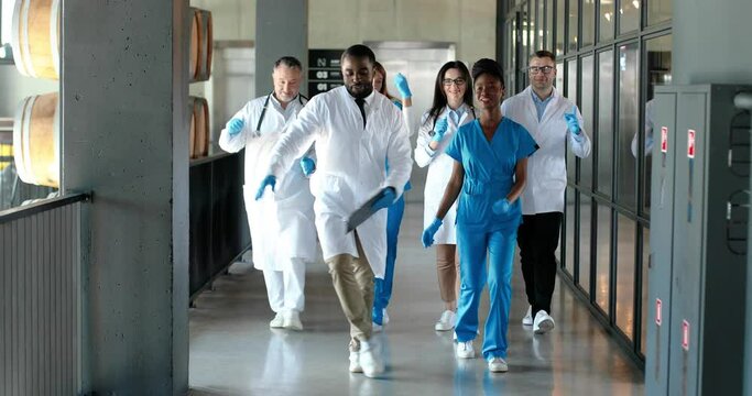 Mixed-races team of males and females doctors and nurses walking and dancing funny at corridor of hospital. Multi ethnic medics in medical uniforms dance and doing fun moves in clinic. Docs having fun