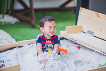 Asian cute baby boy sitting in a sandbox and playing sand, Good for sensory experience and learning by touch their fingers and toes through sand,Active learning concept.