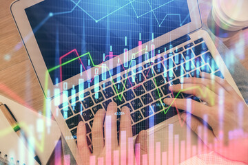 Double exposure of man's hands typing over computer keyboard and forex graph hologram drawing. Top...