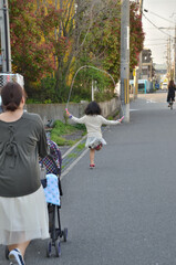 夕暮れに乳母車押す母親と縄跳びをする娘