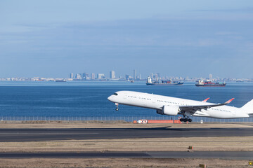 青空を背景羽田空港を離陸する飛行機と東京湾を航行するコンテナ船