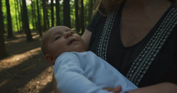 A young mother is cradling her little baby in a forest on a sunny summer day
