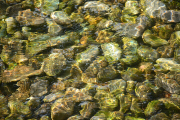 water surface of calm river, small waves, stones and rocks on the bottom