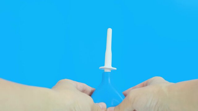 Hand with a blue enema puming, injecting water on a blue background