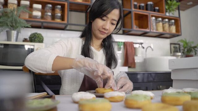 young Asian women wearing aprons and gloves while decorating various donuts with layers of chocolate on the table