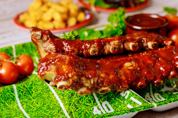 Baked juicy barbecue pork ribs with tomato, sauce and potato for football party.