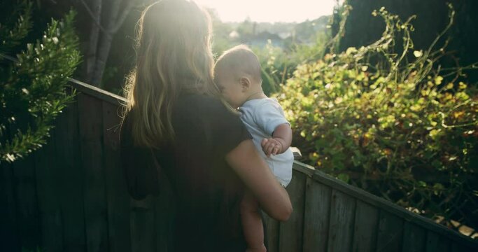 A young mother is holding her baby in the garden at sunset