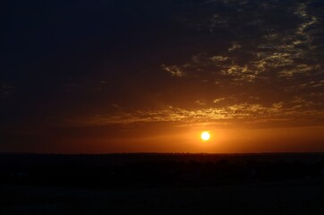  Orange sky with pearl clouds, and a flying silhouette of a bird. At sunset, with a white circle.