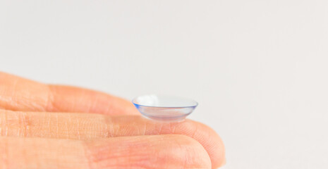 Contact lens on human hand on grey background. Selective focus. Close up