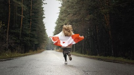 A girl in a white sweater and skirt walks through the forest holding the flag of canada