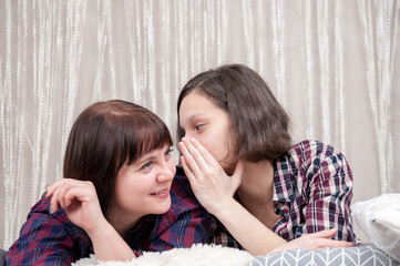 A woman and a girl share a secret on the bed at home, the concept of communication between generations