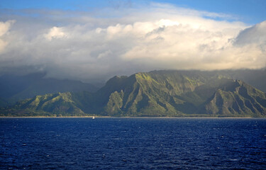 The Napali rugged coastline Hawaii, a small yacht is dwarfed by the dynamic rocky coast.