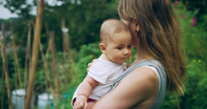 A young mother is standing in her garden holding her baby in the summer