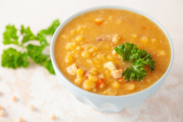 Pea soup with pieces of bacon and parsley in blue bowl on a white background.