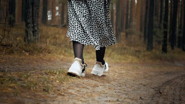 A girl in a dress and a white sweater walks through the forest