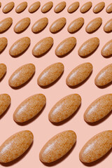 Drug pattern. Repetition of light brown pills on a pink background. Textured background of pills lying in a row. Health concept.