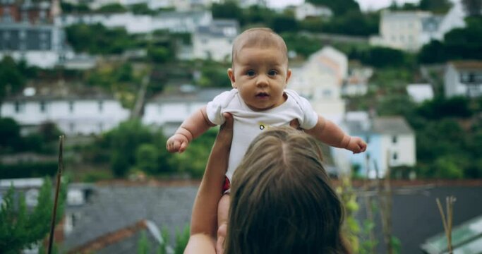 A young mother is lifting up her baby in a garden overlooking a small town