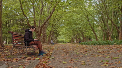 Fototapeta premium Young man sitting with a laptop in the park .serious teenage, guy, young man, student working on laptop in the park. Remote work and learning concept
