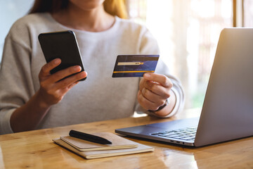 Closeup image of a woman holding credit card while using smart phone and laptop in office